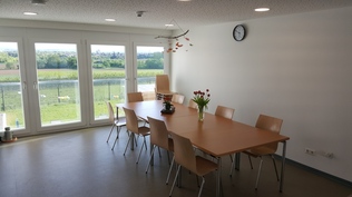 Bild vom Essbereich: Tisch mit Stühlen vor großen Fenstern